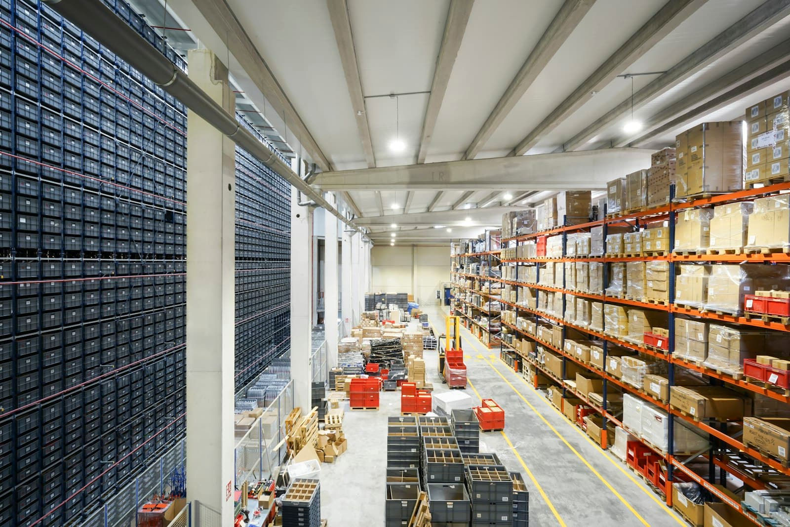Allée de picking d’un entrepôt : rayonnages garnis de cartons de part et d’autre, sol marqué au sol.